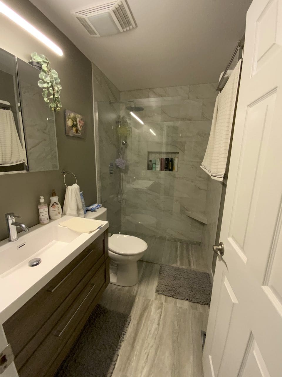 A hallway bathroom remodel featuring marble tile, a wooden floating vanity, and a curbless shower.