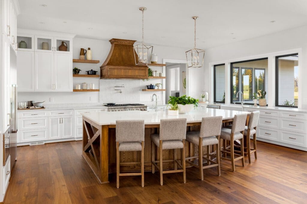 A large, luxury kitchen with white countertops, white base cabinets, and a wooden hood and island.