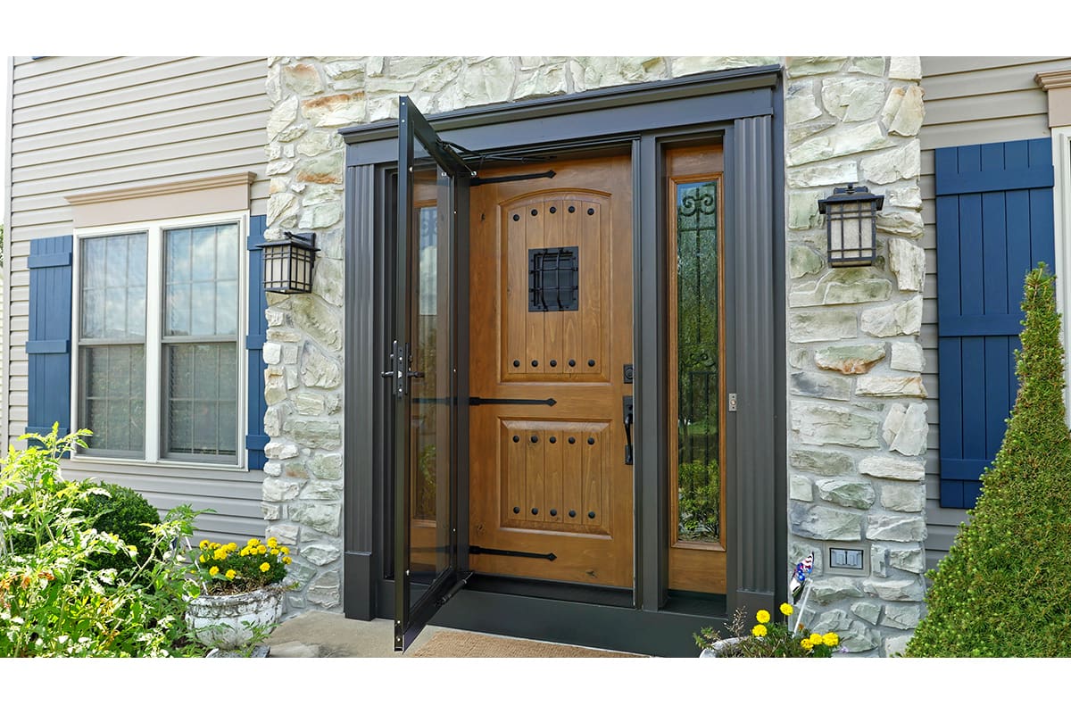 A front door in a slightly dark brown color with dark grey features such as a speakeasy window and rivets.