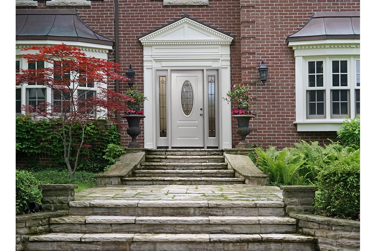 A luxurious front door to a home covered in red brick, with a stone walkway leading up to it.